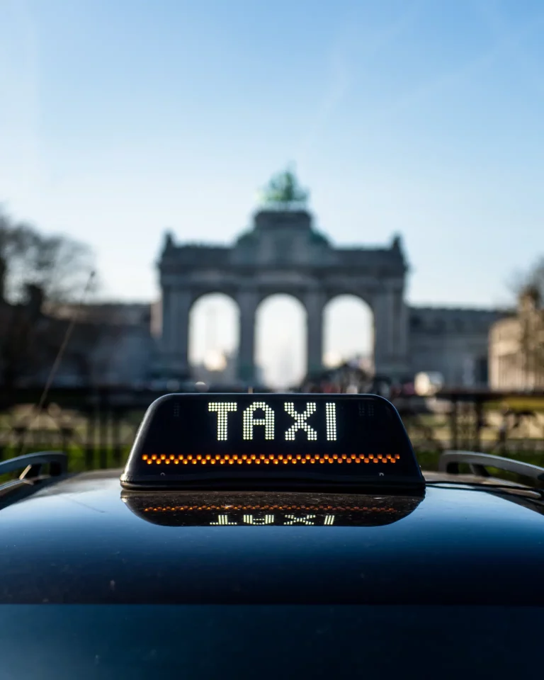 A taxi sign on top of a car, facing the Cinquentenaire Jubilee Park in Brussels
